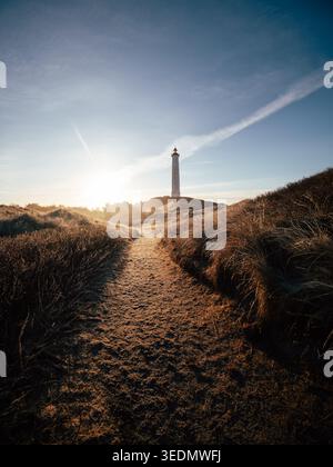Sentier de sable à travers les dunes côtières menant à un phare au lever du soleil. Calme matin. Banque D'Images