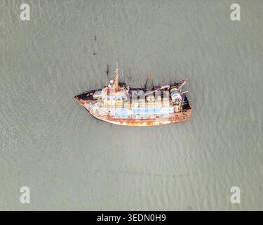 Vue aérienne d'un chalutier de pêche bleu rouillé et orange flottant sur une eau calme et trouble. Banque D'Images