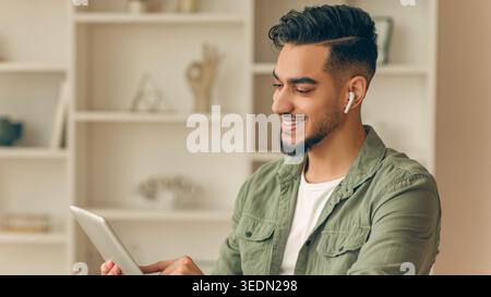 Jeune homme utilisant une tablette tout en portant des écouteurs sans fil à la maison pendant la journée Banque D'Images
