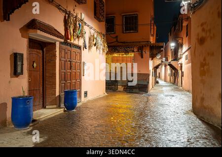 Vue nocturne atmosphérique d'une rue étroite de la médina de Marrakech au Maroc avec des portes traditionnelles en bois, des pots en céramique bleue, des poivrons séchés suspendus et Banque D'Images