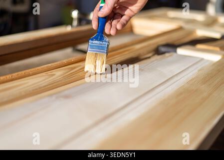 Gros plan de la personne appliquant un vernis de protection ou une tache de bois avec un pinceau sur les nouvelles portes en bois. Amélioration de la maison, travail du bois, rénovation et bricolage c Banque D'Images