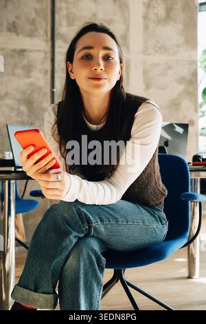 Portrait de jeune femme d'affaires tenant le téléphone tout en étant assis sur la chaise au bureau Banque D'Images