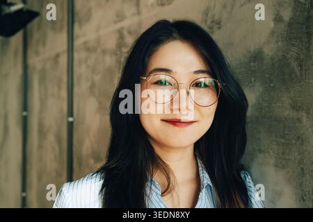 Portrait de jeune femme d'affaires souriante appuyée sur le mur au bureau Banque D'Images