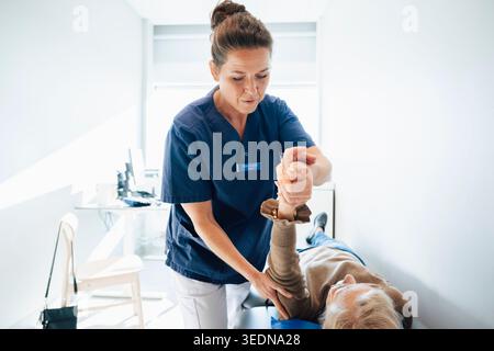 Physiothérapeute féminine étirant la main d'un patient allongé sur la table dans la salle d'examen à l'hôpital Banque D'Images