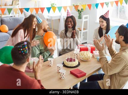 Groupe de jeunes amis heureux et divers réunis autour de la table pour célébrer l'anniversaire et profiter de la fête. Banque D'Images