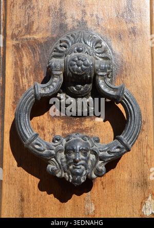 Frappeur de porte orné antique avec un visage sculpté sur une porte en bois rustique Banque D'Images