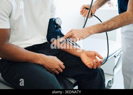 Médecin masculin vérifiant la pression artérielle du jeune homme tout en utilisant stéthoscope sur le bras pendant l'examen médical dans la chambre à l'hôpital Banque D'Images