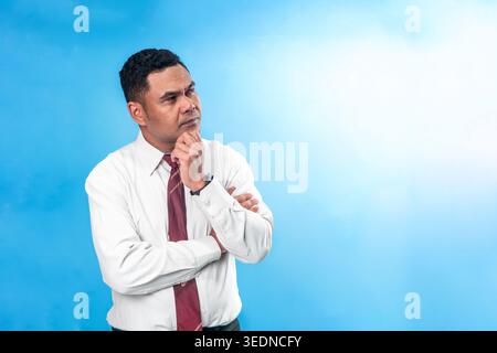 Portrait d'un employé de bureau indonésien pensif en chemise blanche et cravate, tenant son menton tout en réfléchissant profondément. Concept de résolution de problèmes et d'idées. Banque D'Images