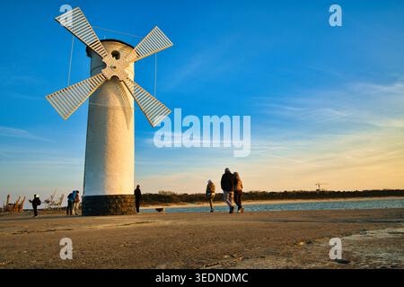 Couple marchant le long de la promenade côtière près de White Windmill Lighthouse au coucher du soleil avec d'autres personnes - la ville balnéaire de Świnoujście. Banque D'Images