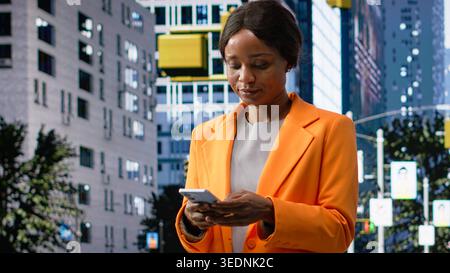 Portrait d'un professionnel noir prenant un appel à distance sur smartphone, marchant dans les rues de la ville. Mouvement flou des personnes reflétant la routine réaliste et l'activité urbaine. Caméra B. Banque D'Images