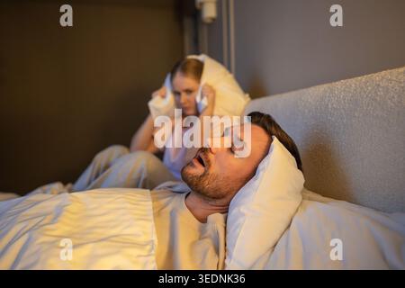 Femme épuisée avec privation de sommeil et insomnie souffrant de ronflement de partenaire la nuit. Banque D'Images