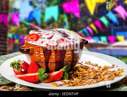 Délicieux bol d'açai garni de fraises fraîches et de lait en poudre, servi avec du granola sur une assiette blanche. Festif flou Festa Junina arrière-plan wi Banque D'Images