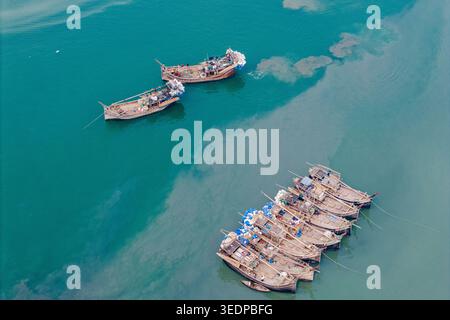 Moheskhali Upazila, Bangladesh - 11 mars 2026 : vue aérienne de bateaux de pêche traditionnels en bois avec des pêcheurs à bord ancrés dans une eau turquoise. Banque D'Images