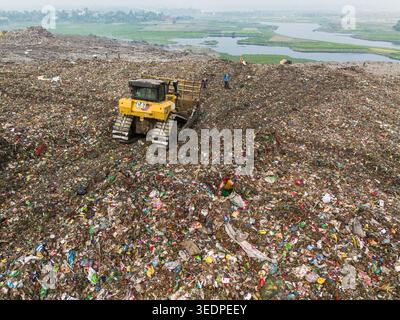 Aminbazar, Bangladesh - 26 janvier 2025 : vue aérienne d'un bulldozer jaune transportant des déchets à la décharge d'Aminbazar avec des ouvriers fouillant entre les piles Banque D'Images