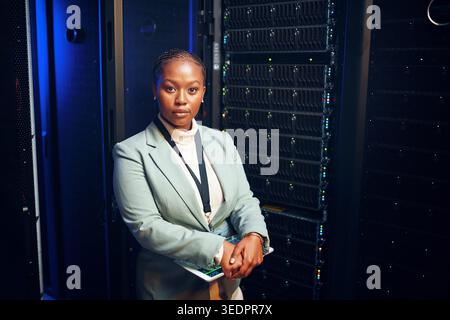 Portrait, femme noire et sérieuse avec programmeur dans la salle du serveur pour l'inspection, la cybersécurité et le codage. Technicien, tablette et centre de données pour Banque D'Images