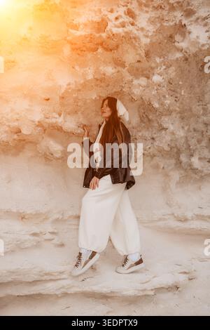 Femme nature de falaise blanche explorant au coucher du soleil tout en portant des vêtements décontractés élégants et debout près de murs de roche de sable Banque D'Images
