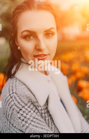 Portrait de jardin de coucher de soleil de femme montre une belle jeune femme souriant dans un champ de tulipes oranges pendant l'heure dorée Banque D'Images