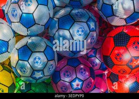 Plusieurs ballons de football en plastique gonflables groupés ensemble dans un filet blanc mince. Les boules présentent diverses couleurs vives, y compris le bleu, le rouge, le rose. Banque D'Images