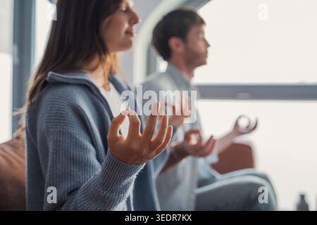 Couple conscient méditant ensemble pratiquant le yoga assis dans la pose de lotus sur le canapé à la maison, calme homme paisible et femme respirant de l'air sur le canapé pour maintenir la santé physique mentale et l'équilibre émotionnel Banque D'Images