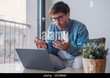Un homme d'affaires caucasien amical en tenue décontractée parle sur un appel vidéo portable dans le bureau, souriant et saluant tout en dirigeant une conférence en ligne ou une réunion d'affaires virtuelle Banque D'Images