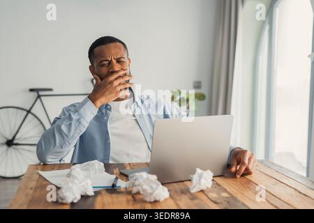 Jeune homme biracial frustré, massant la tête après avoir échoué à travailler, se sentant fatigué en raison du surmenage informatique. Homme afro-américain du millénaire dépassé et stressé souffrant de surmenage et de surétude Banque D'Images