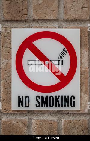 Panneau non-fumeur monté sur un mur de briques brunes, montrant un symbole d'interdiction rouge sur une icône de cigarette. Banque D'Images