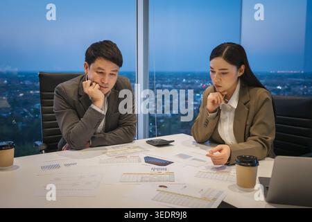 Les partenaires commerciaux sérieux se sentent stressés et réfléchissent lorsqu'ils analysent des documents lors d'une réunion nocturne dans un bureau de grande hauteur Banque D'Images