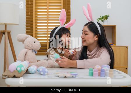 mère et fille d'enfant préscolaire portant des oreilles de lapin tenant l'oeuf coloré tout en célébrant ensemble à leur maison le jour de pâques. joyeuses vacances en famille a Banque D'Images