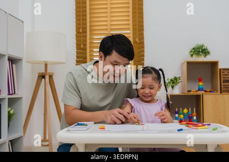 père et enfant fille dessin et peinture avec des pastels à l'huile colorés sur papier à la maison Banque D'Images