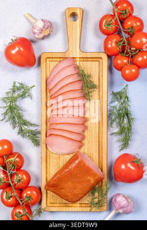 Longe de porc fumée, tranchée et entière, reposant sur une planche à découper en bois, entourée de tomates mûres de vigne, tomates simples, aneth frais et bu à l'ail Banque D'Images
