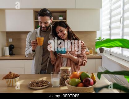 Un homme et une femme prennent leur petit déjeuner dans une cuisine. Ils se sourient tout en partageant nourriture et boissons à table. Banque D'Images