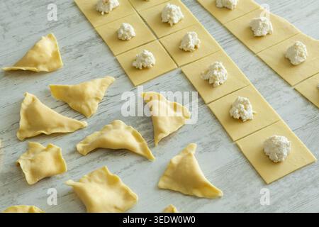 Carrés de pâte à pâtes avec garniture de fromage blanc et raviolis pliés sur une surface en bois. Banque D'Images
