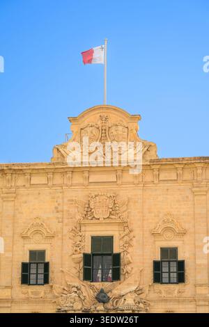 Le drapeau maltais flotte au sommet de l'Auberge de Castille (bâtiment baroque) contre un beau ciel bleu d'été à la Valette, Malte. Banque D'Images