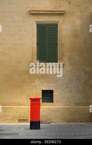 Une boîte aux lettres rouge traditionnelle avec une architecture de bâtiment en calcaire en arrière-plan à la Valette, Malte. Banque D'Images
