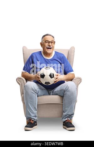 Homme senior expulsé assis dans un fauteuil tenant un ballon de football isolé sur fond blanc Banque D'Images