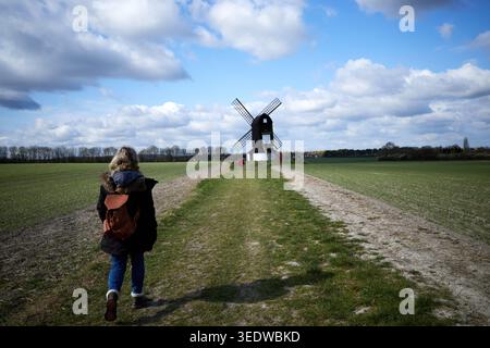 Une femme portant un sac à dos marron marche vers Pitstone Windmill dans le Buckinghamshire. Devant vous se trouve un petit garçon vêtu d'un manteau rouge. Banque D'Images