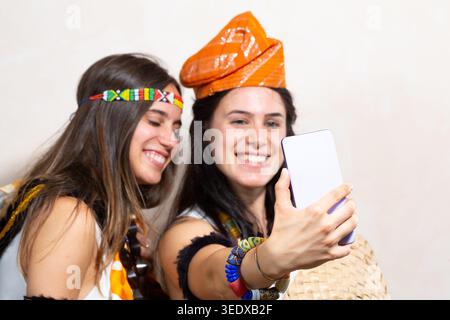 Deux jeunes femmes amies prenant selfie avec smartphone, portant des costumes ethniques colorés Banque D'Images