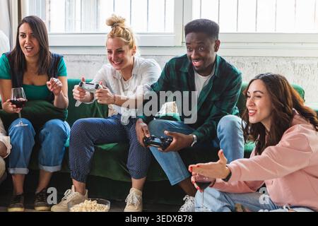 Amis divers jouant à des jeux vidéo et s'amusant ensemble à la maison avec des collations Banque D'Images