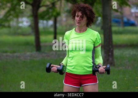Femme exerçant à l'extérieur faisant des boucles de biceps avec des haltères Banque D'Images