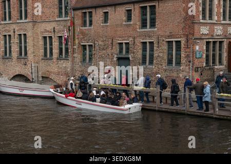 Bruges, Belgique - 3 avril 2026 : les touristes montent à bord de bateaux sur le canal à Rozenhoedkaai près de bâtiments historiques en briques et de la promenade du front de mer. Activité touristique Banque D'Images