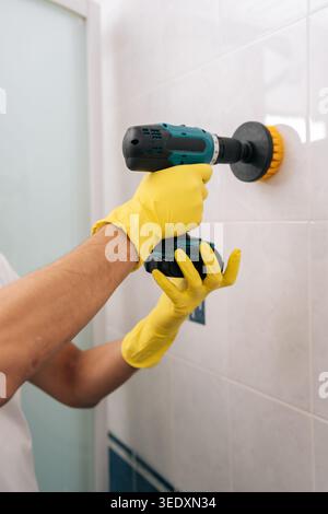 Plan vertical recadré d'un homme à l'aide d'une puissante perceuse à récurer électrique pour nettoyer efficacement les carreaux blancs de salle de bain, accélérant ainsi les tâches ménagères de routine avec Banque D'Images