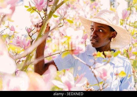 Femme africaine entourée de fleurs de Magnolia rose dans Dreamy Spring Garden Banque D'Images