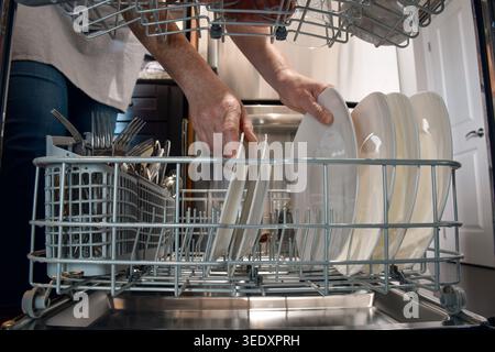 Femme déchargeant de la vaisselle propre du lave-vaisselle vu de l'intérieur de l'appareil. Corvée quotidienne à la maison avec point de vue perspective, mettant en évidence domestique Banque D'Images