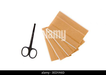 Ciseaux et bandes adhésives beiges disposées sur un fond blanc, représentant les soins médicaux ou le toilettage personnel Banque D'Images