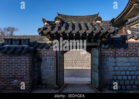 Porte voûtée traditionnelle avec toit carrelé orné, ouverte dans un mur de pierre et de brique, palais Gyeongbokgung, Séoul, Corée du Sud Banque D'Images