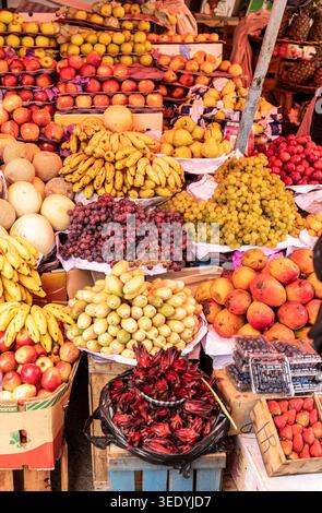 Des bananes, des pommes, des raisins, des mangues et des poires encombrent un étal de fruits sur un marché en plein air à Sucre, en Bolivie, à côté de caisses de myrtilles et de fraises Banque D'Images