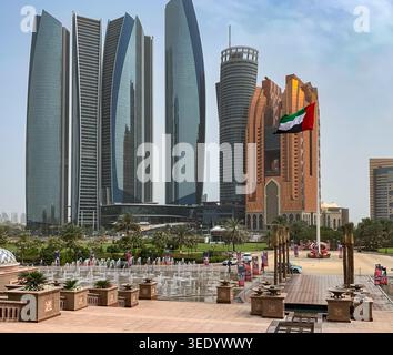 Vue sur les gratte-ciels modernes et un drapeau des Émirats arabes Unis agitant donnant sur une place avec des fontaines, des palmiers et des gens à Abu Dhabi, Abu Dhabi, Émirat arabe Uni Banque D'Images