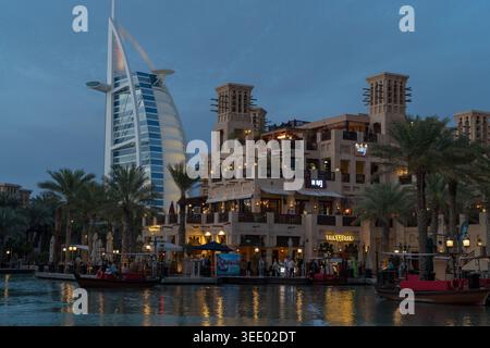 Vue sur l'hôtel de luxe Burj Al Arab et Madinat Jumeirah bâtiments traditionnels avec des palmiers et des bateaux sur l'eau au crépuscule à Dubaï, Dubaï, Unite Banque D'Images