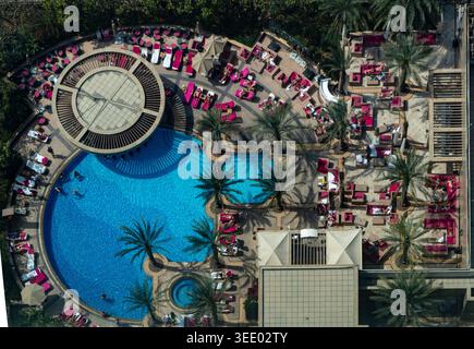 Vue sur la piscine d'un complexe hôtelier de luxe avec de l'eau turquoise, des palmiers et des personnes se relaxant sur des chaises longues roses à Dubaï, Dubaï, Émirats arabes Unis Banque D'Images