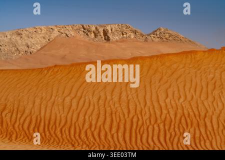 Vue sur les dunes de sable rouge avec des ondulations de vent et une crête de montagne rocheuse sous un ciel bleu clair dans le désert Dubaï, Dubaï, Émirats arabes Unis. Banque D'Images